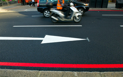 road with a single red line, white arrow pointing right and a motorbike and car in the background